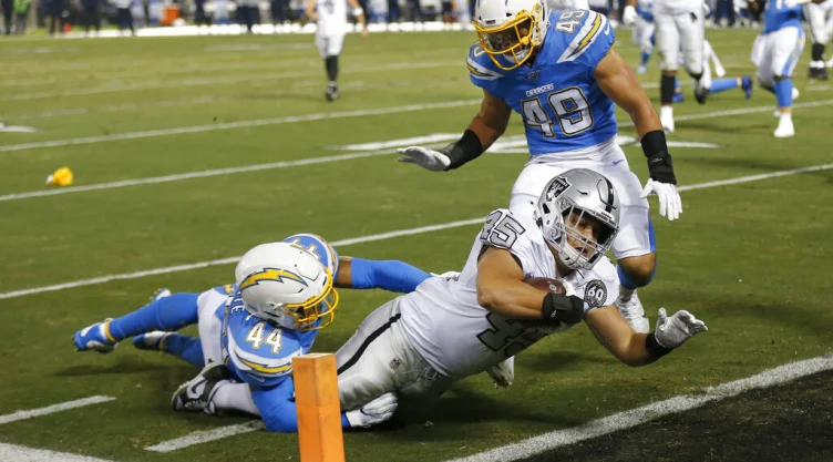 El running back de los Raiders de Oakland Alec Ingold consigue una anotación al superar a los linebackers de los Chargers de Los Ángeles Kyzir White y Drue Tranquill (49) en la primera mitad del juego del jueves 7 de noviembre de 2019, en Oakland,