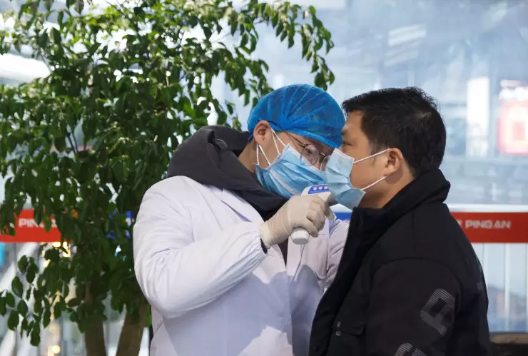 Un trabajador de salud toma la temperatura corporal a un hombre en la sala de embarques del aeropuerto de Changsha, en la provincia de Hunan, como medida de precaución debido al brote de coronavirus. Enero 27, 2020.  REUTERS/Thomas Peter
