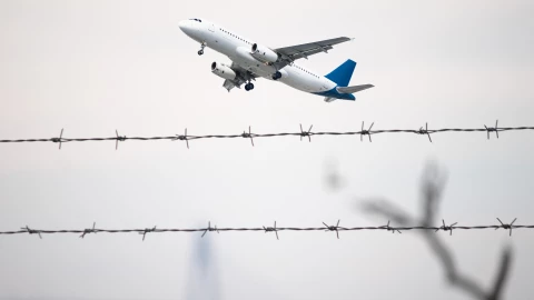 Un avión sobrevuela una valla de alambre.