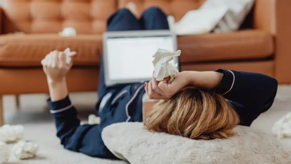 Mujer enferma de gripa con pañuelos en mano y trabajando desde casa.