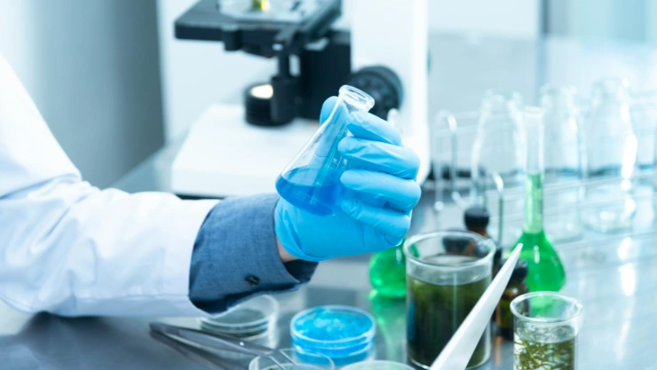 Laboratorista con guante azul sujeta un recipiente con un líquido azul en laboratorio.