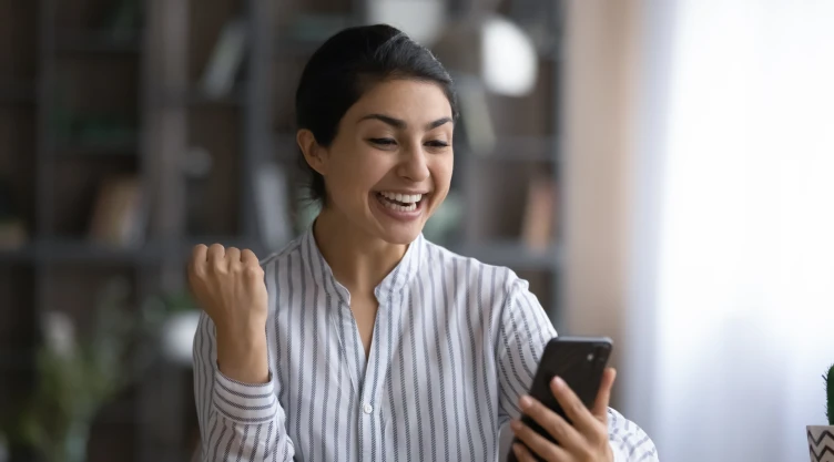 Una mujer se muestra emocionada al leer una notificación en su teléfono.