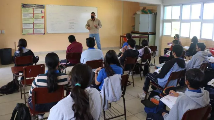 Alumnos tomando clases sentados en sus pupitres frente a su docente.