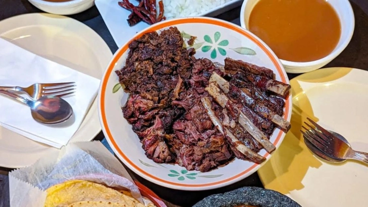 Plato de carne de chivo con sus pequeñas costillas, acompañadas de salsas mexicanas y los cubiertos