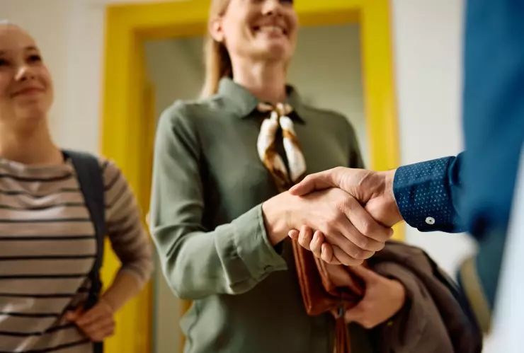 Una madre junto a su hija estudiante le estrecha la mano a un docente