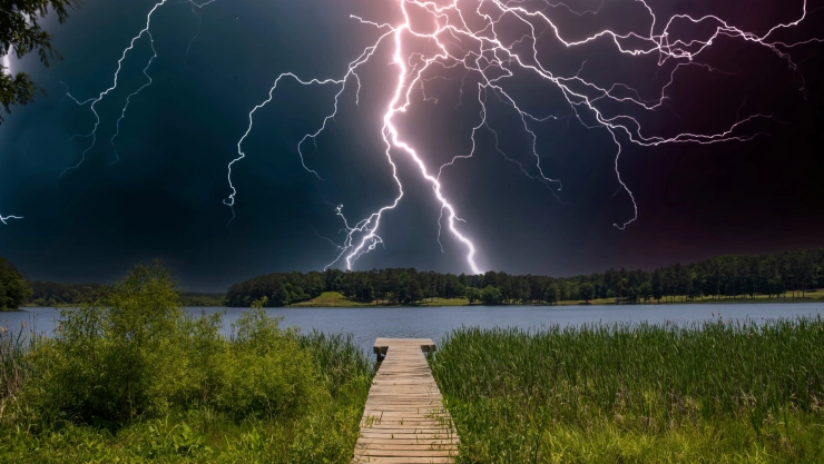 Un rayo cayendo desde el cielo en el anochecer tormentoso, detrás de un lago y la vegetación