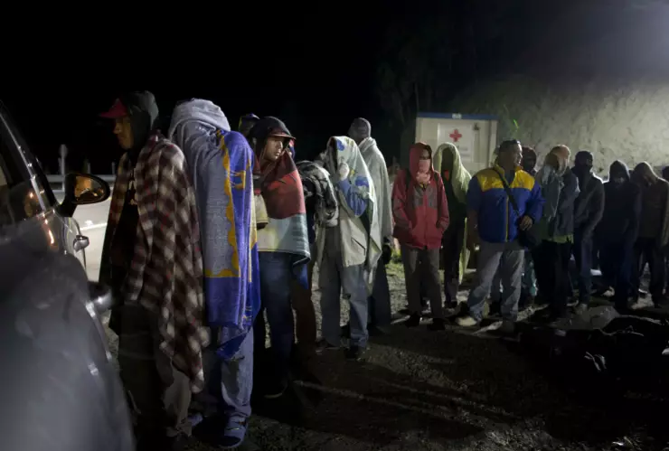 Migrantes venzolanos hacen fila para recibir pan y café que reparte una familia colombiana desde su auto, en una gasolinera en Pamplona, Colombia. Imagen, AP.