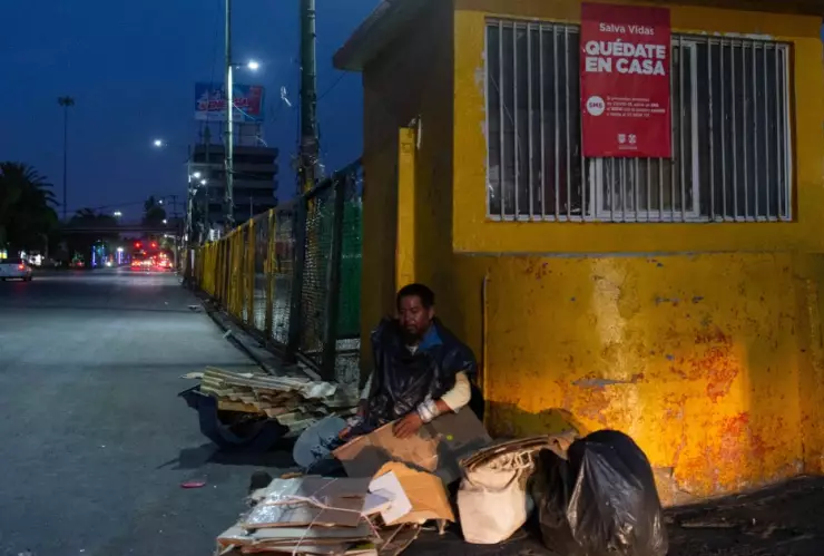 Hombre en situación de calle en la cdmx frente un anuncio de Quédate ne Casa por el COVID-19