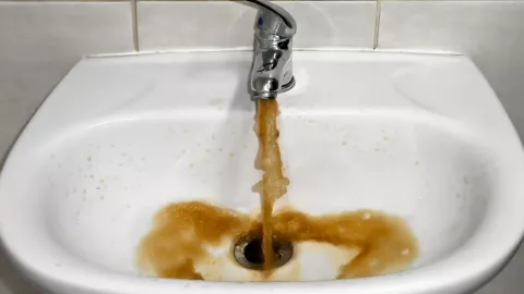 Agua sucia color tierra saliendo del lavamanos de un baño