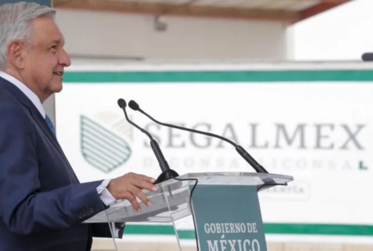 El expresidente de México, AMLO hablando por micrófono, con el logo de Segalmex de fondo.