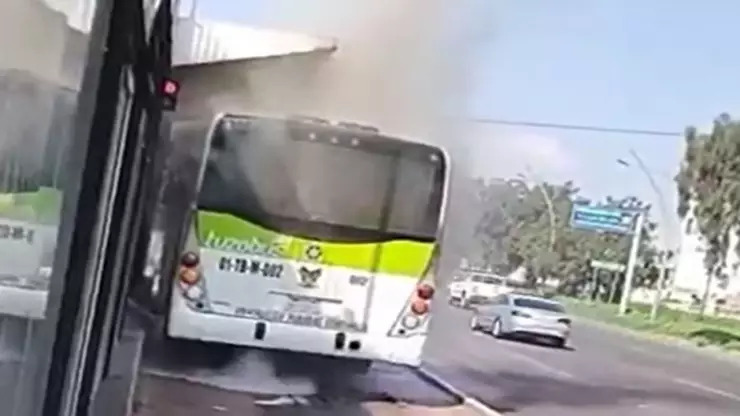 Arde Tuzobús tras incendio por falla mecánica frente a plaza comercial en Pachuca. En la imagen se observa cómo la unidad vehicular Tuzobús es cubierta por humo tras un incendio en el interno por una falla mecánica. Ante esta situación, los pasajeros son desalojados en la estación.