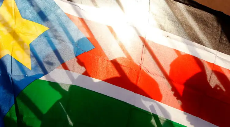 Siluetas de habitantes de Sudán del Sur vistas a través de una bandera de ese país.