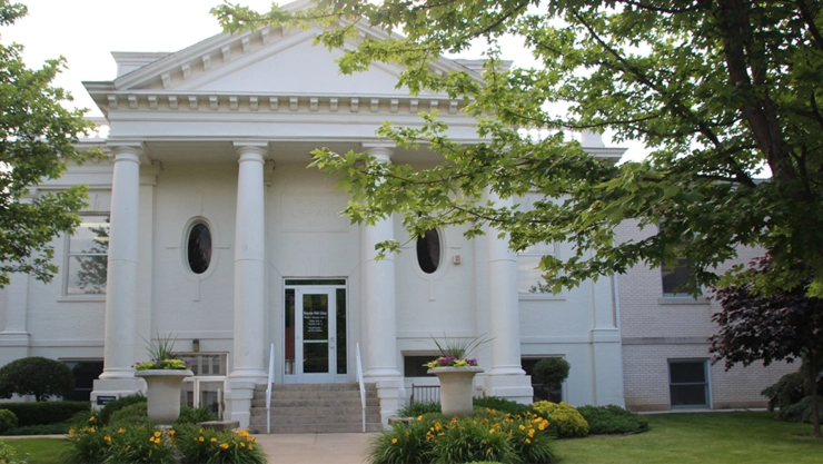 Fachada principal de una biblioteca en un pueblo de Illinois, con sus columnas blancas y el parque verde prolijo en la entrada