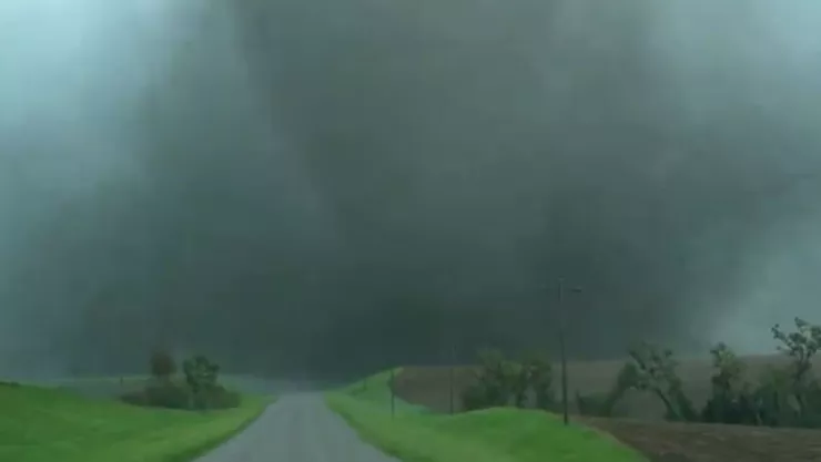 Un tornado se ve al fondo del camino de una carretera en el campo.