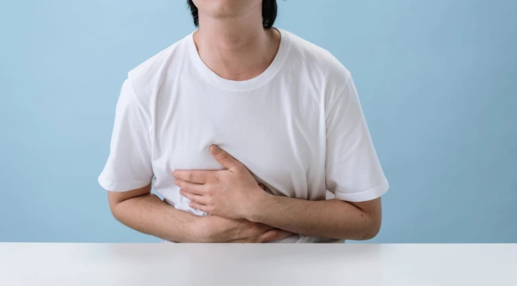 Joven con playera blanca tocándose el pecho por dolor.