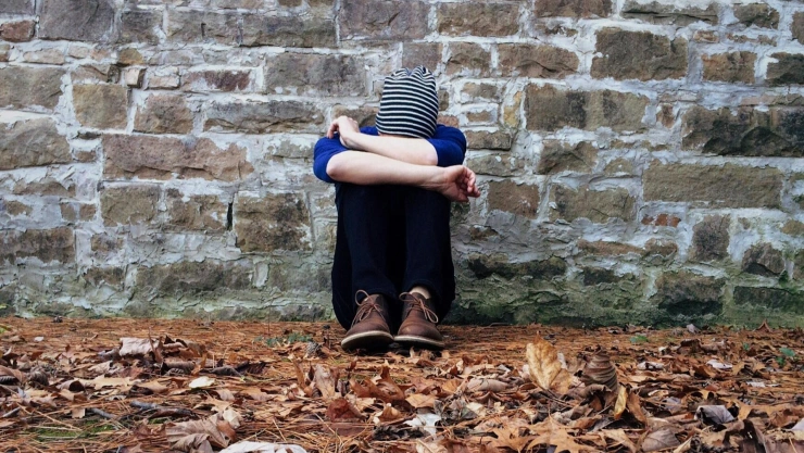 Persona sentada, de aspecto triste, abrazando sus piernas
