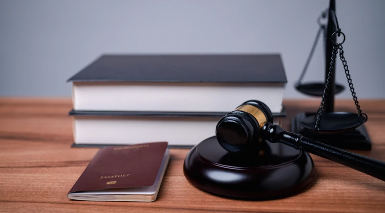Un pasaporte sobre una mesa, al lado de unos libros y un mazo.
