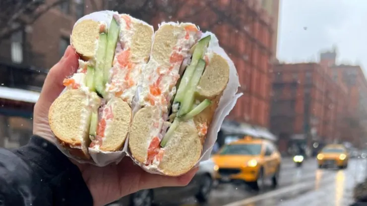 Una mano sostiene un bagel con el fondo de la ciudad de Nueva York.