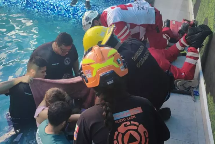 Rescatan a niña atrapada en tubería dentro de alberca en Guadalupe, NL. En la imagen se observa cómo elemento de Protección Civil, Bomberos y familiares tratan de rescatar a la menor atrapada.