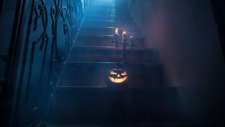 Una calabaza con y un candelabro están en una escalera de una casa embrujada.