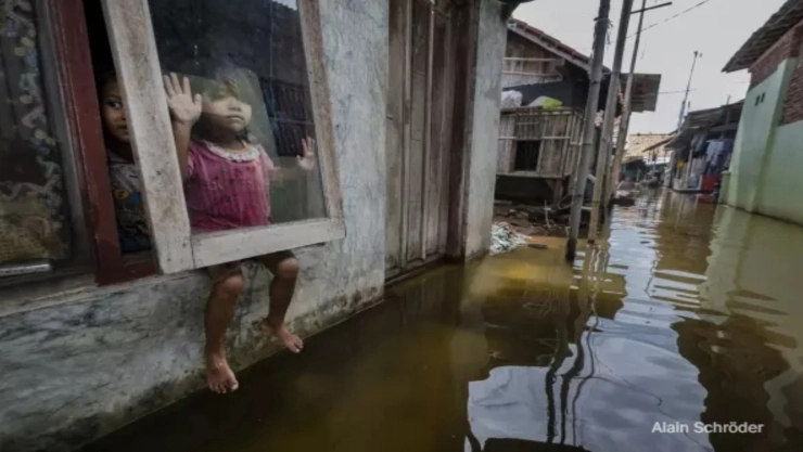 Una niña mira por una ventana en Yakarta, Indonesia, una calle inundada.