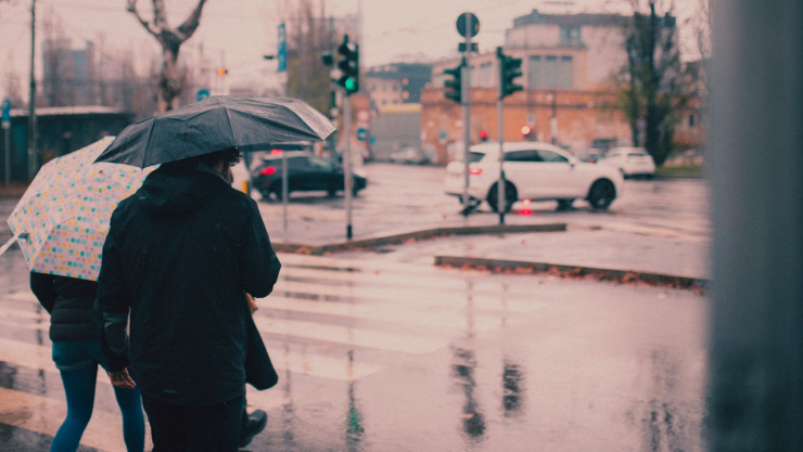 Personas caminando bajo la lluvia en la ciudad con paraguas en mano.