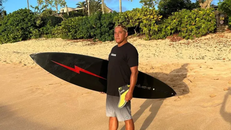 Tamayo Perry en una playa con una tabla de surf