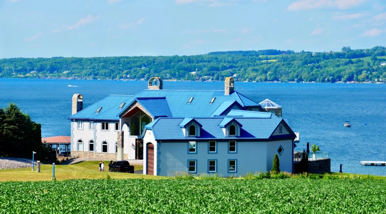 Una casa grande con techo de tejas azules, a la vera del lago y un parque de césped verde y prolijo