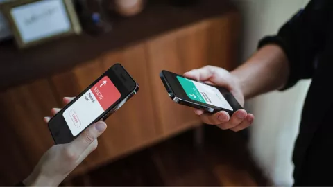 personas sosteniendo sus celulares, en la pantalla se refleja el envío y recibo de una transferencia bancaria