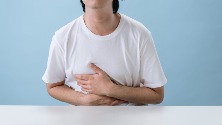 Joven con playera blanca tocándose el pecho por dolor.