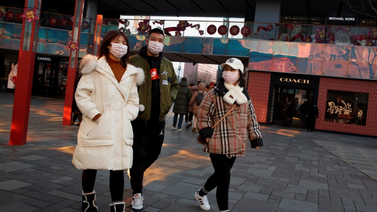 People wearing face masks walk past luxury boutiques in the Sanlitun shopping district in Beijing