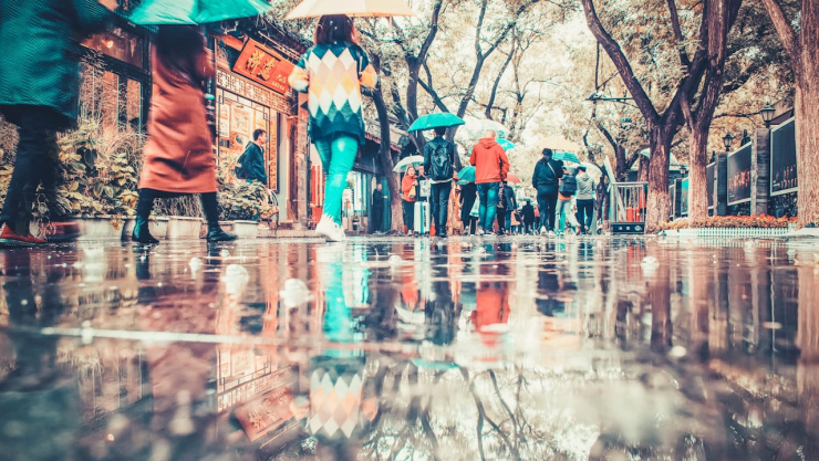 Personas caminando bajo la lluvia en la ciudad con un espejo de agua.