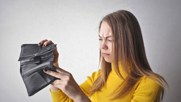 Mujer con blusa amarilla observa su cartera con confusión, pues la deuda es mayor que sus ingresos.