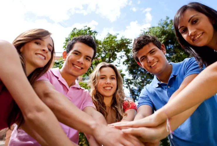 Un grupo de cinco personas al aire libre une sus manos en el centro