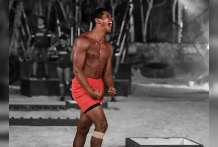 Atleta sin playera con short rojo gritando durante una competencia en la playa